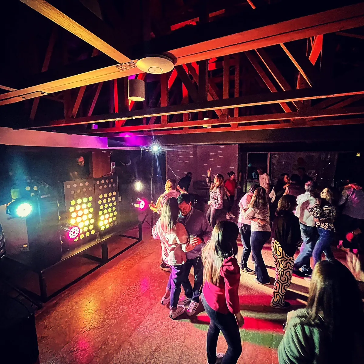 Invitados bailando en una fiesta en casa con DJ y luces de colores